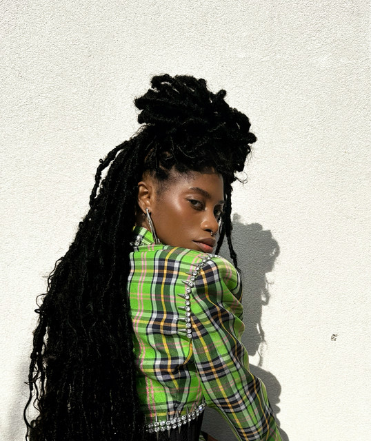 Attis in a green plaid jacket against a white wall